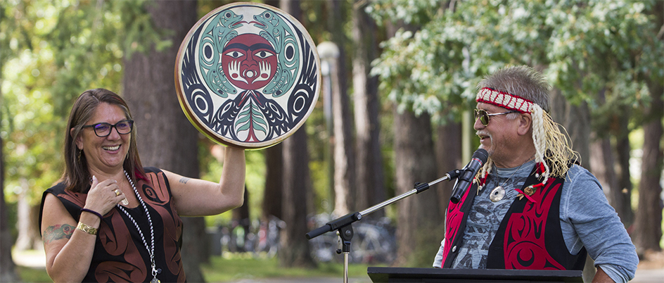 Robina Thomas holding up a drum as the artist, TEMOSEṈ, describes it