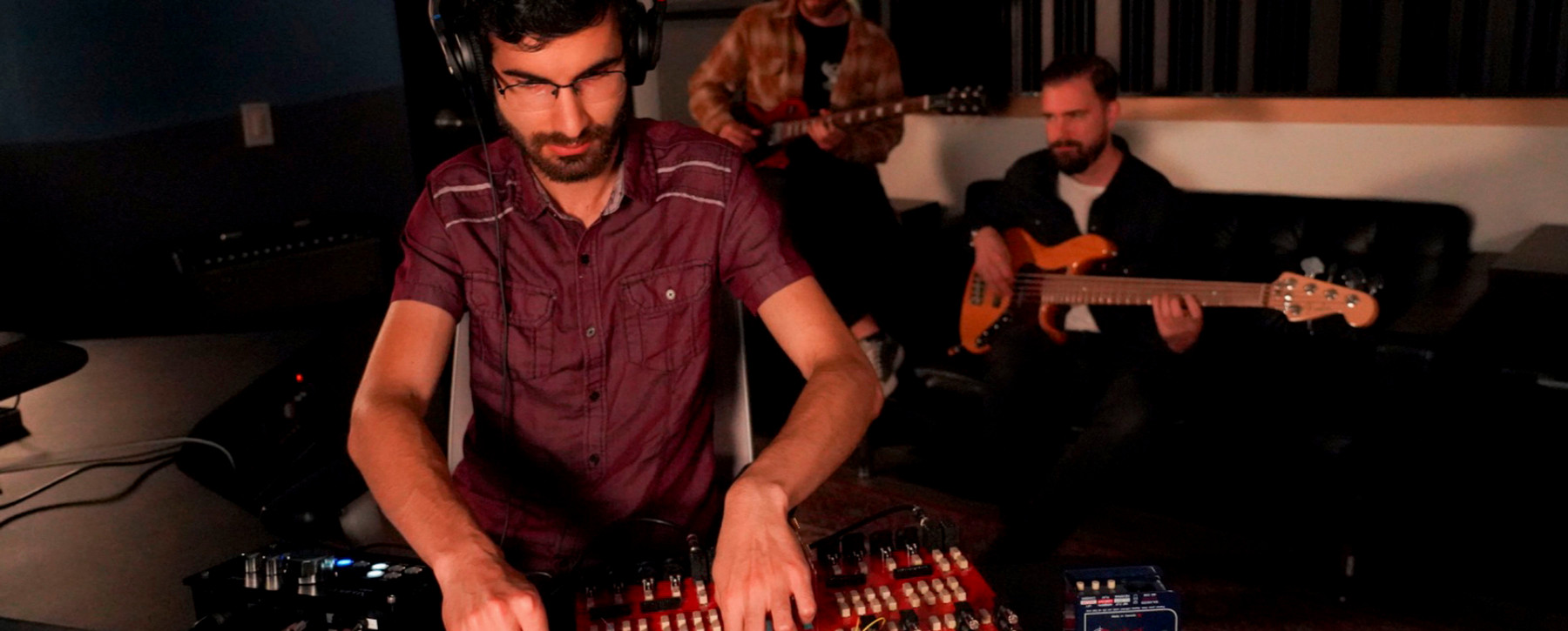 A student uses a sound mixer board while another student plays guitar in the background.