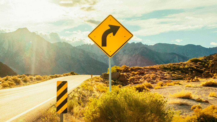 A photo of a right-turn road sign beside a sunny road.