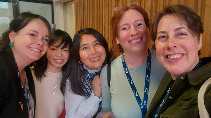 Five people pose for a photo and smile at the camera.