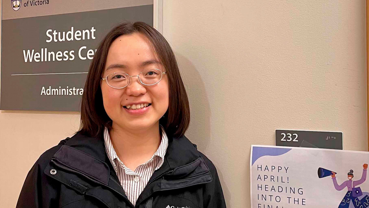 A student stands in front of a sign saying Student Wellness Centre.