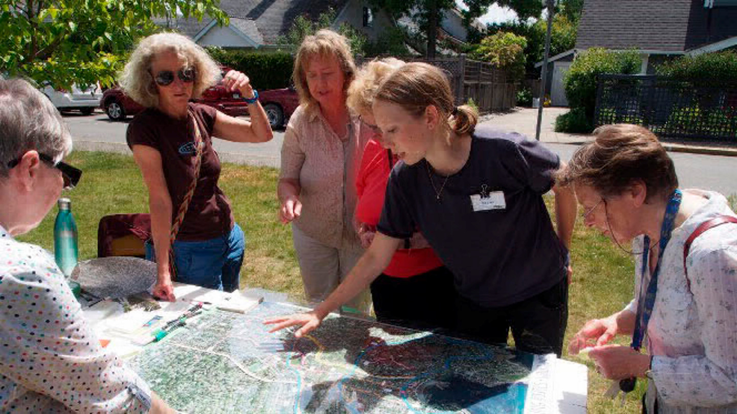 A group of students and community members talk around a table outside.