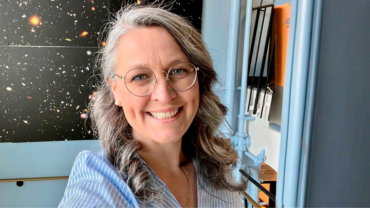 A woman with grey hear stands in front of a poster showing the stars.