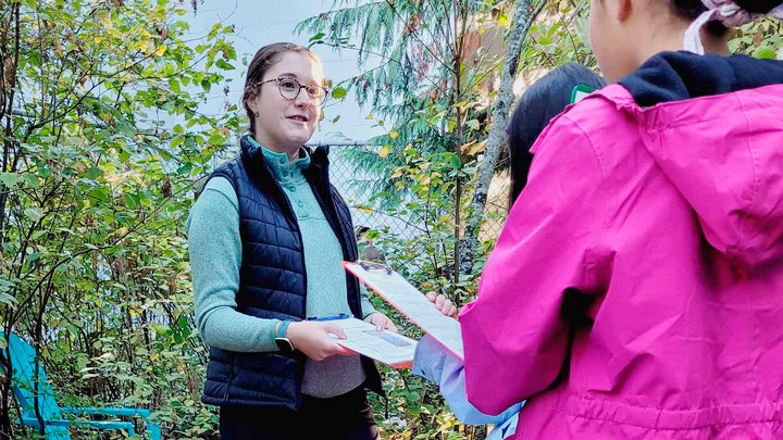 A student stands in a forest and speaks to a group a people.