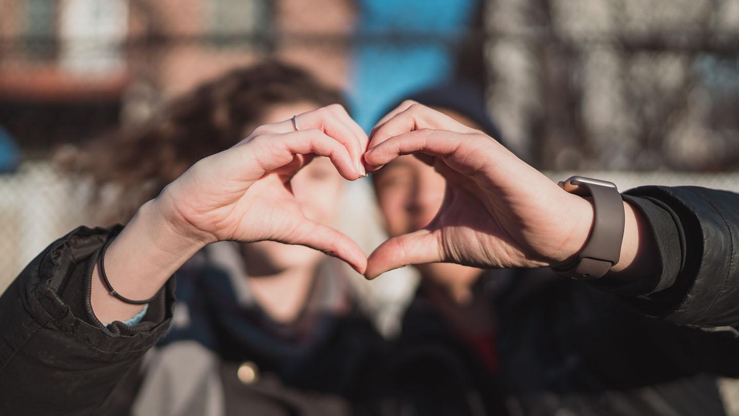 Two students hold their hands in front of their faces to form a heart.