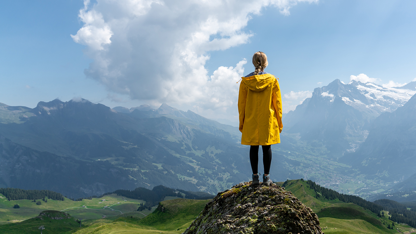 A student wearing a yellow jacket stands at the top of the mountain, facing away from the camera.