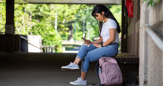 Student sitting on his dorm bed looking at his phone