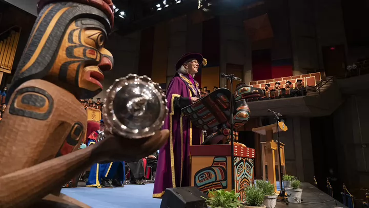 A delegate speaking to new graduates surrounded by traditional and Indigenous furnishings