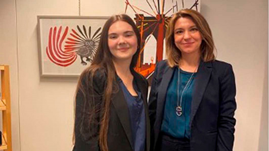 A student stands with their employer in front of some artwork.