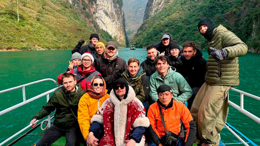 A group of people sit on a boat with a river and mountains behind them.