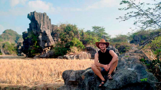 A student sits on a rock in front of an open field.