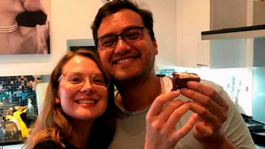 Two people stand close together in an apartment.