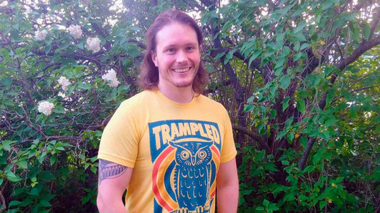 A student stands in front of a bush.