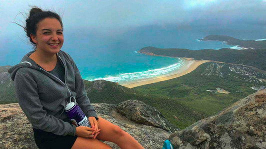 A student sits at the top of a hill overlooking a beach.