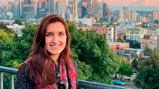 A student smiles while standing on a balcony.