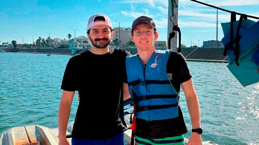 Two students stand on a dock. One wears a life jacket.