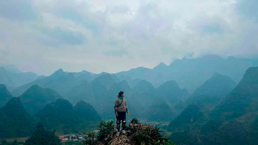 A student standing on top of a mountain with other mountains in the distance.
