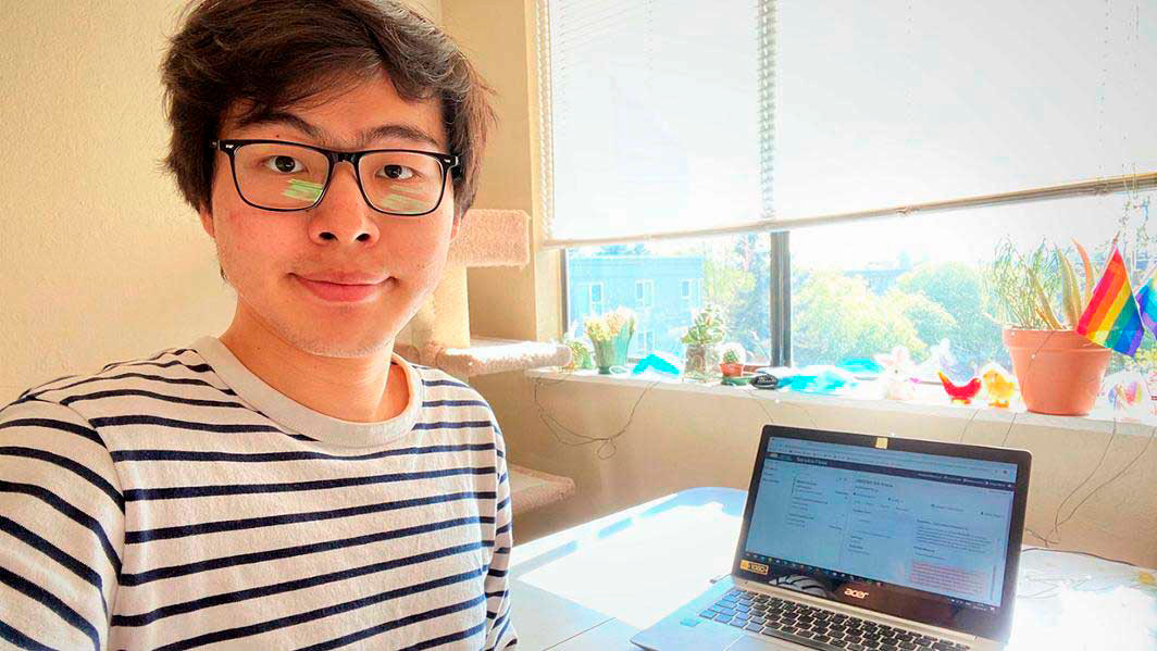 A student wearing a striped shirt sits at a desk in front of a laptop.