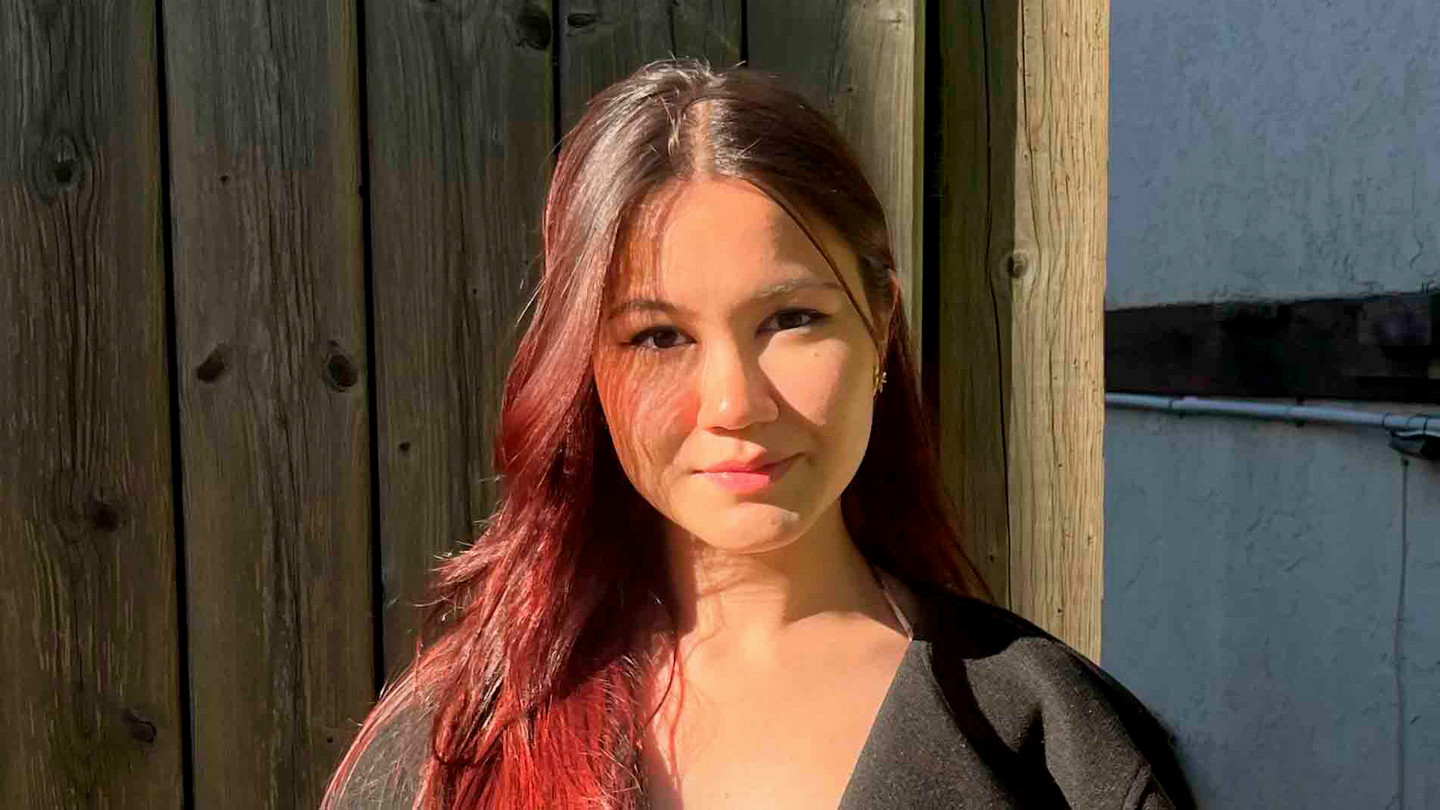 A student with long hair smiles at the camera.