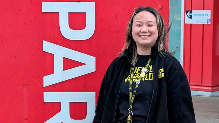 A student wearing a lanyard stands outside of Science World.