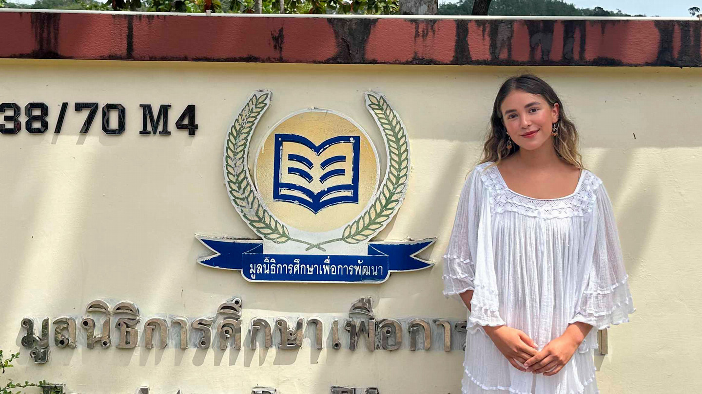 A student stands in front of a sign in Thailand.