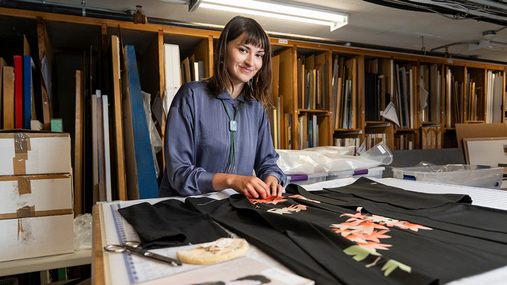 A student sews a garment in a museum setting.