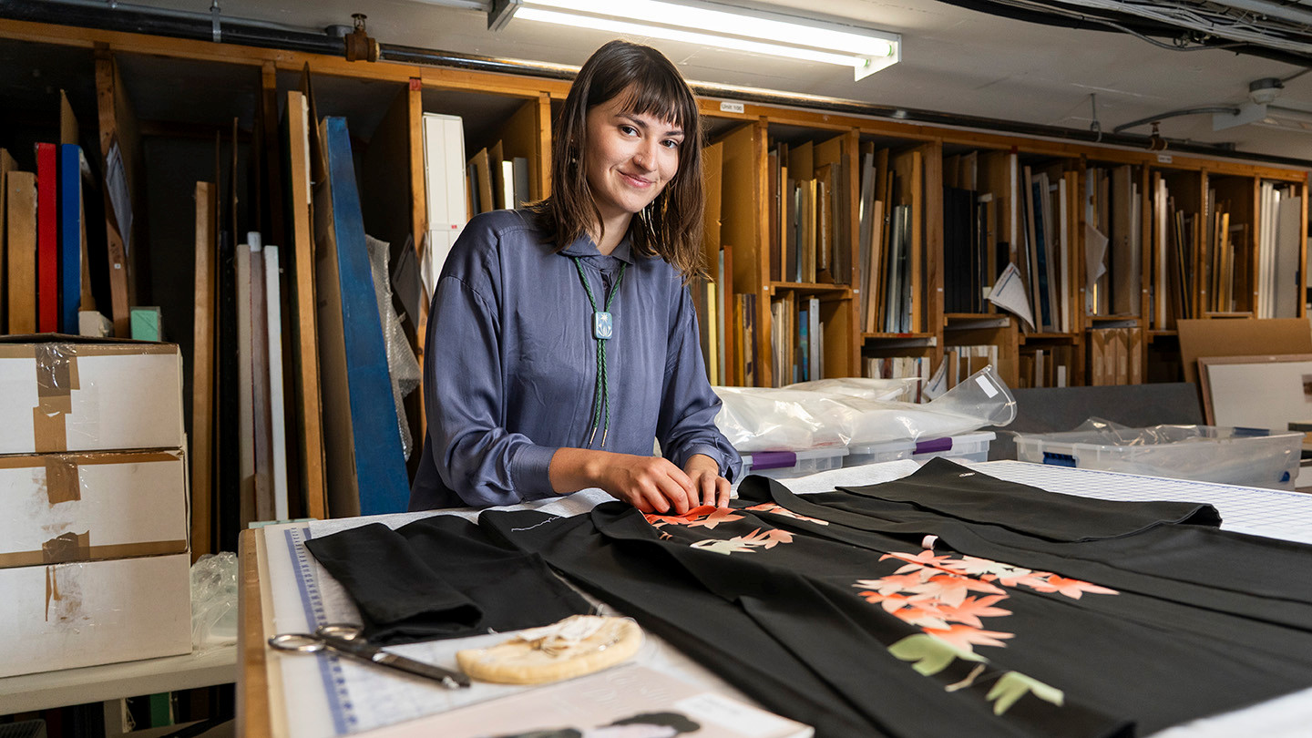 A student sews a garment in a museum setting.