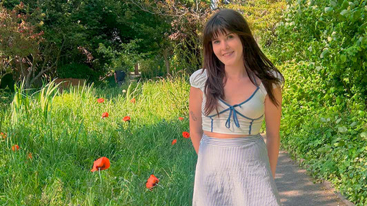 A student stands on a path beside tall grass and wild poppies.