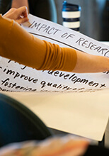 Researcher holding up large paper pad with the words "Impact of Research"