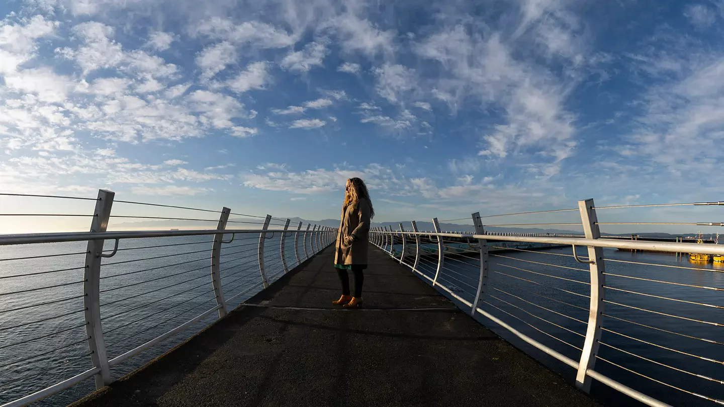 A person stands on Victoria's Breakwater path looking out at the ocean.