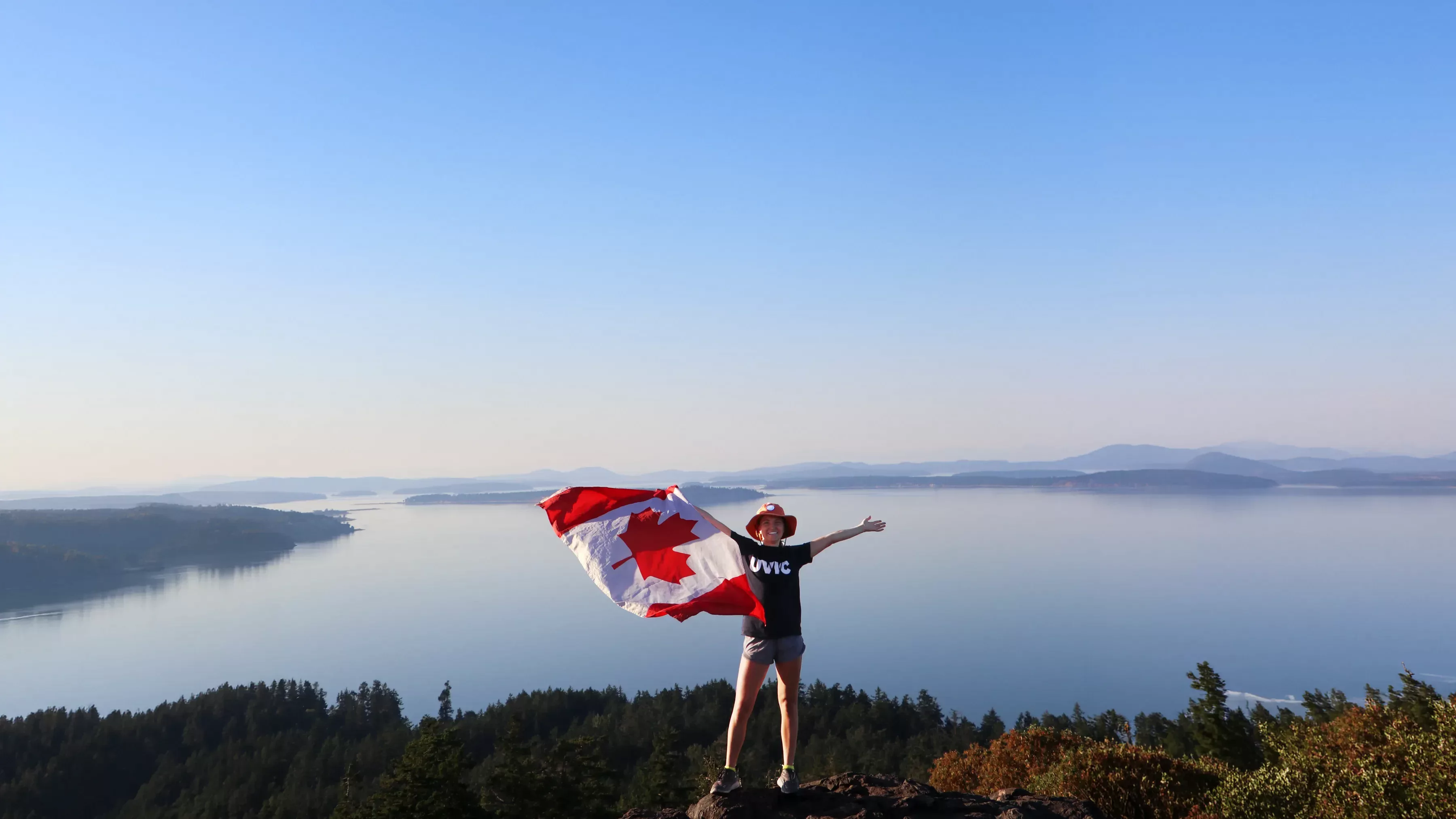 A student standing on top of a mountain holding a Canada flag.
