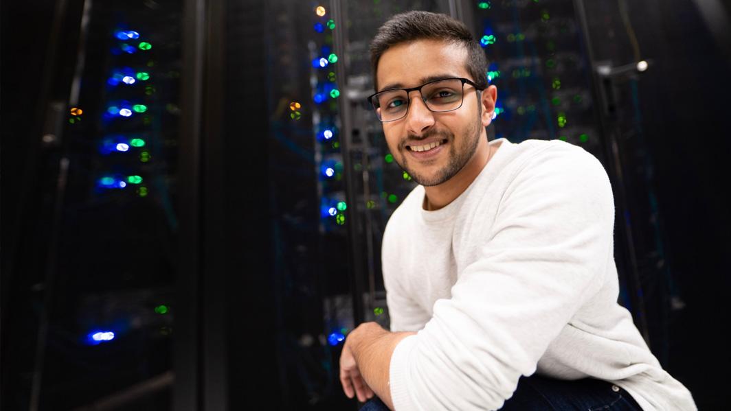 Kodituwakku stands in front a rack of computer servers, which glow with colourful lights.