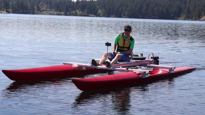 Alec Krawciw sits on a catamaran that is floating in the water.