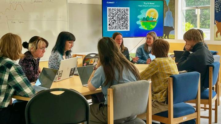 Several people sit around a table in a classroom working together.