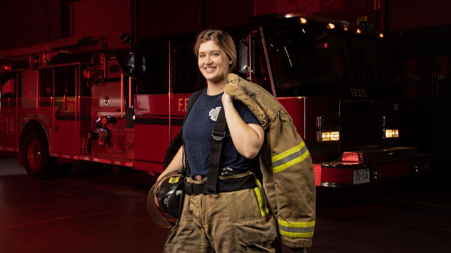 Bradley-Island is shown at night wearing her firefighter gear in front of a firetruck.