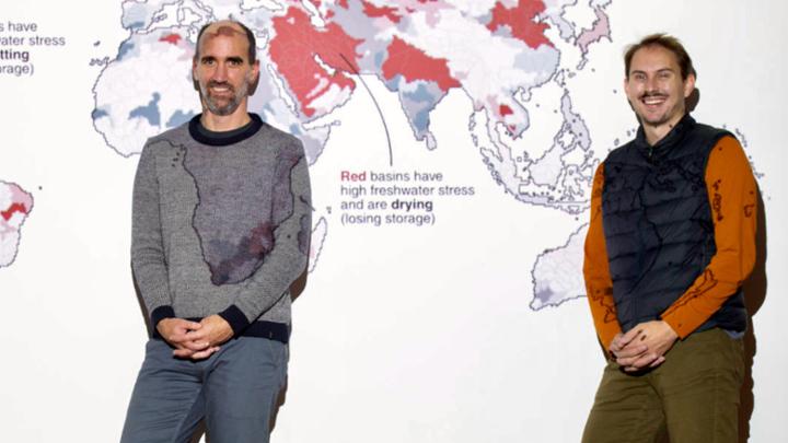 Two people stand in front of a giant screen on which a map of the world is projected, with freshwater basin stress identified by colour.