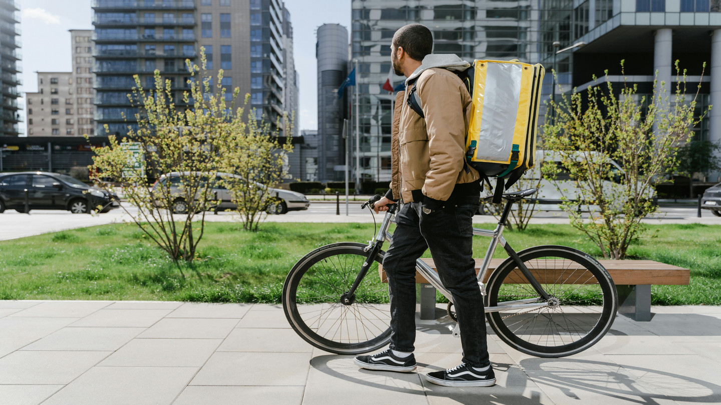 A man wheels a bike past some trees in a city