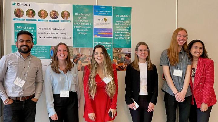 Six people wearing name tags stand together indoors in front of a poster on a wall titled “ClimAct.”