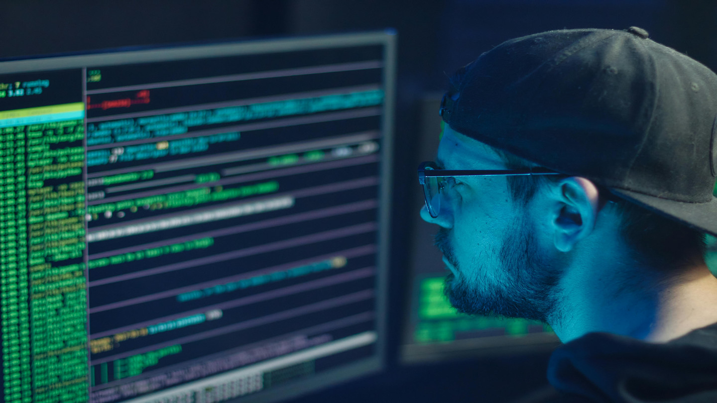 A man wearing a backwards hat looking at a computer screen.