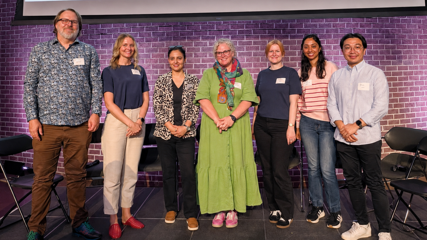 6 researchers stand on stage at a conference.