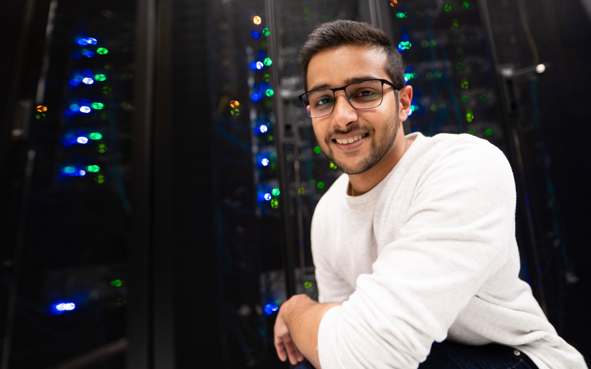 Kodituwakku stands in front a rack of computer servers, which glow with colourful lights.