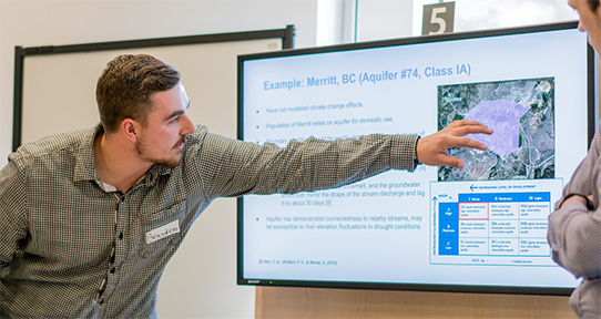 UVic alumnus pointing at a screen with data