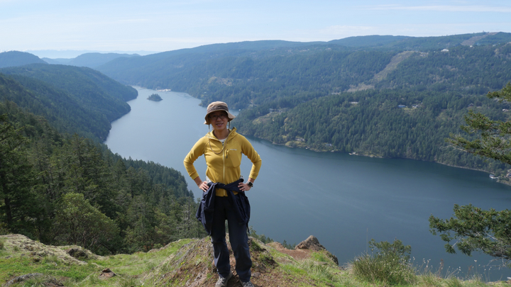 Yu Yan standing at the top of a mountain with a river in the background.