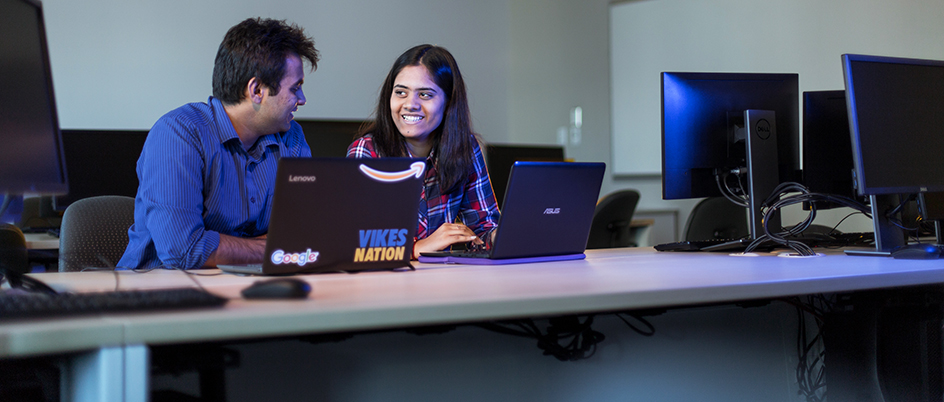 Two UVic students on laptops smiling at each other