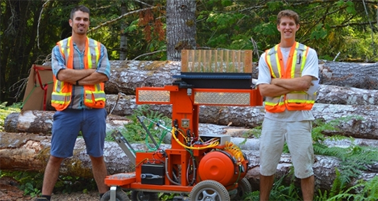 Two UVic students standing outdoors next to their tree-planting robot