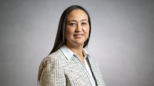 A head-and-shoulders portrait of Dr. Christine Webster in an indoor photo studio. She is wearing a white collared shirt and a cream tweed blazer.