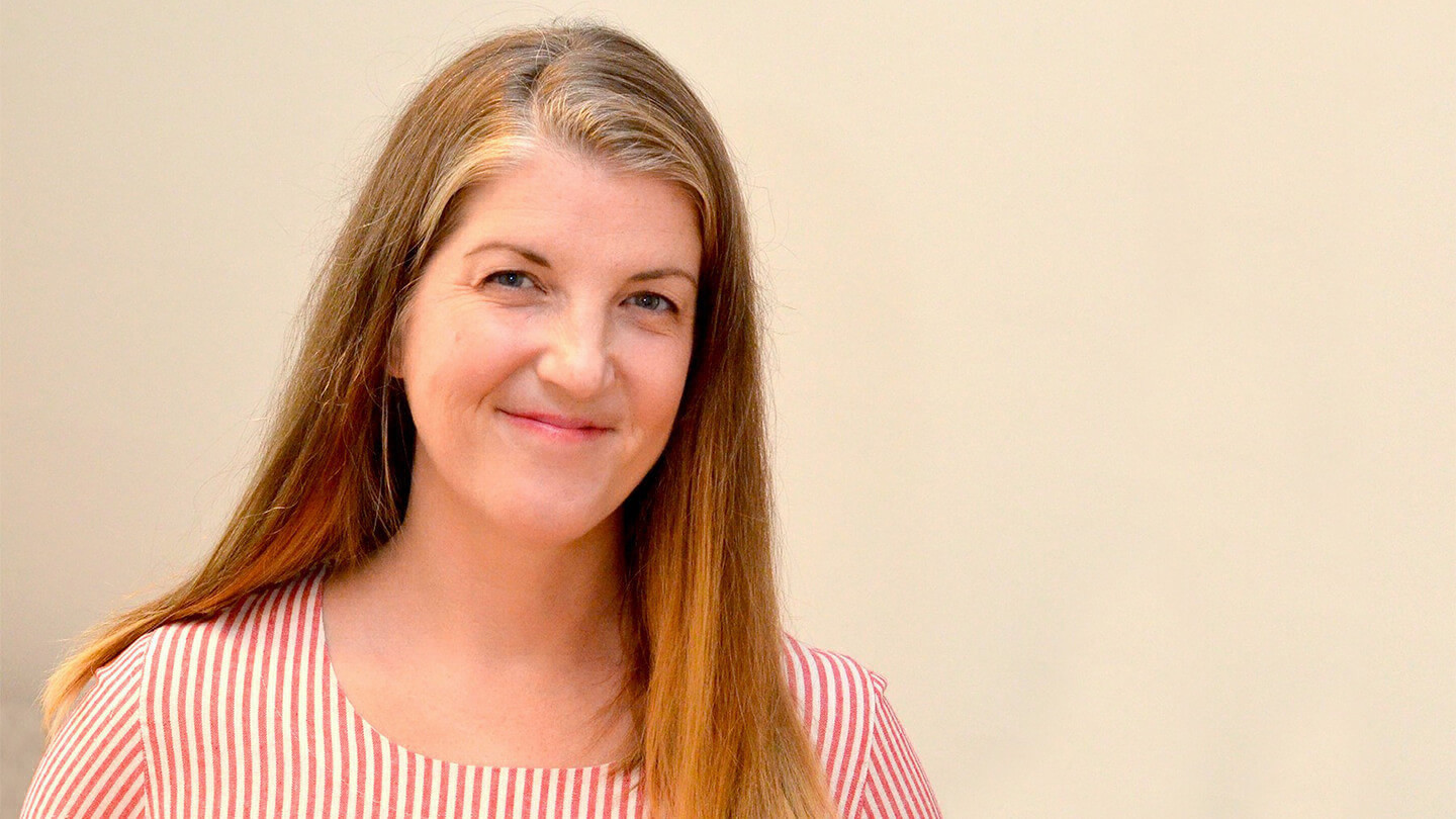 A portrait of alumna Carrie Tennant. She is photographed close-up, indoors, smiling and wearing a striped red and white shirt.