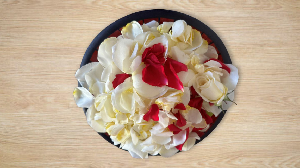 A shallow, black-rimmed bowl of white and red petals is pictured from above, sat upon a wooden surface.