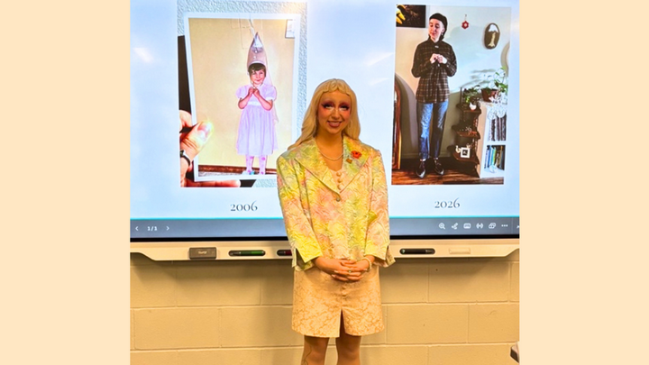 Graham is pictured as their drag character Ella Minnow Pea while presenting at WestCAST conference. they are standing in front of a projector screen which shows a photo of them from 2006 and one from 2026.