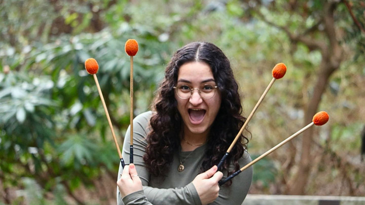 A portrait of Liv posing outside with two sets of mallets.